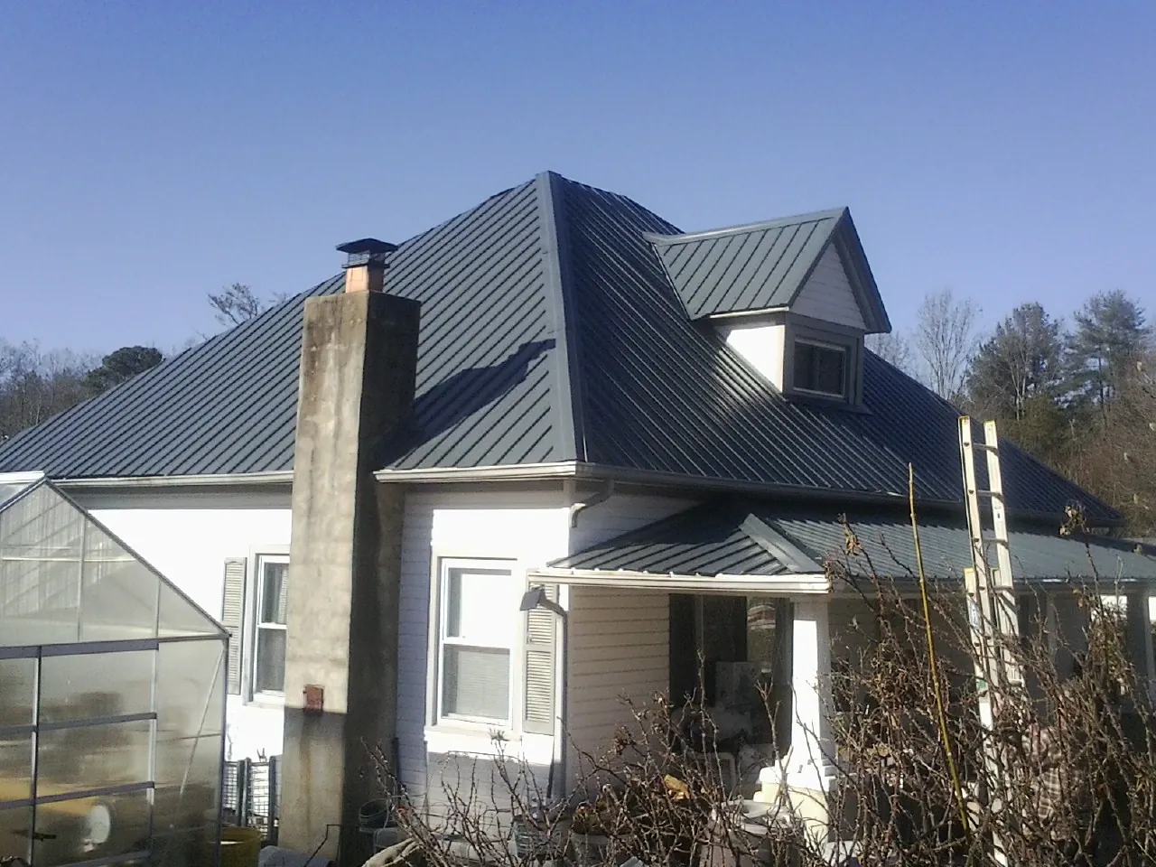 Dark blue standing seam metal roof on a white farmhouse with dormer — Slate & Tile Roof Repair by Roofing Brothers in Commodore