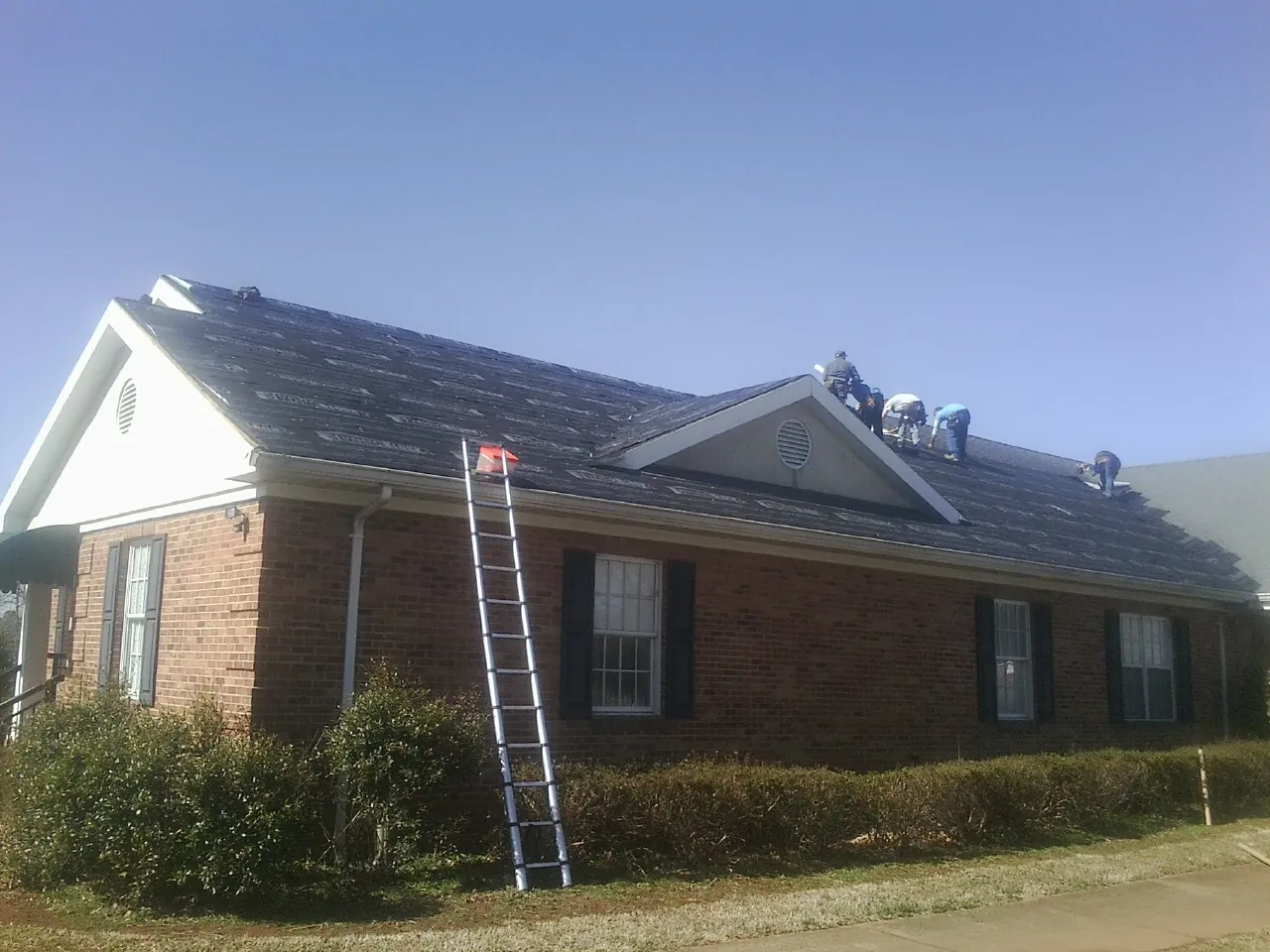Crew tearing shingles off a brick ranch roof with a ladder set — Metal Roof Repair work by our crew in Commodore
