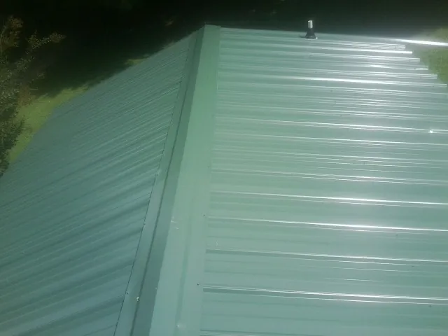 New green metal panels meeting at the ridge of a roof — Flat Roof Repair work by our crew in Commodore