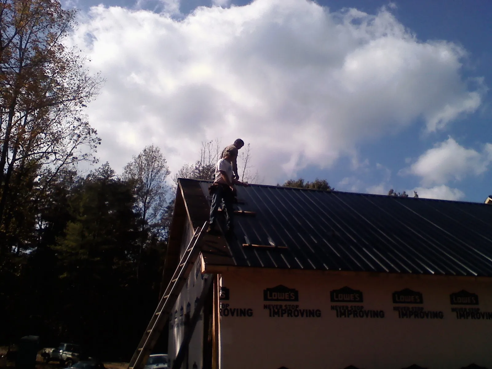 Roofer fastening dark metal panels high against a cloudy sky, from a Roof Inspection job in Commodore