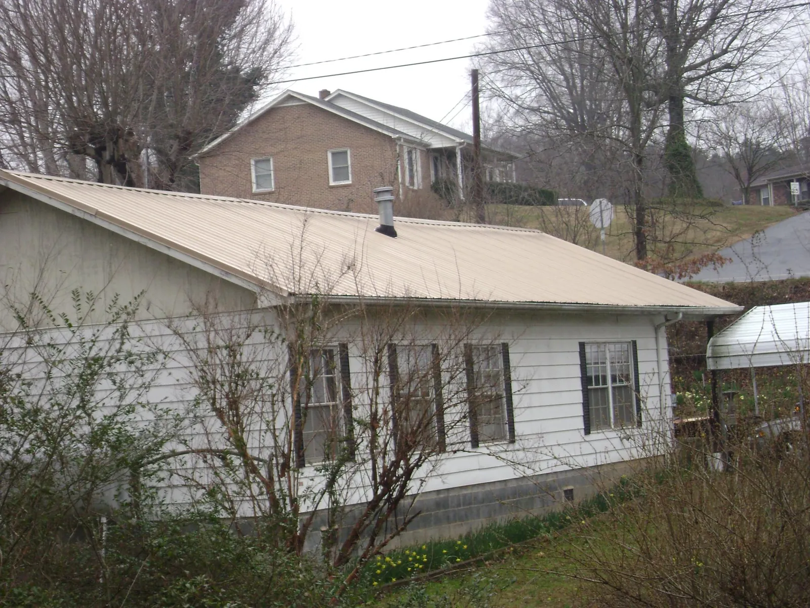 Tan metal roof on a white sided house set into a hillside — Commercial Roofing by Roofing Brothers in Commodore